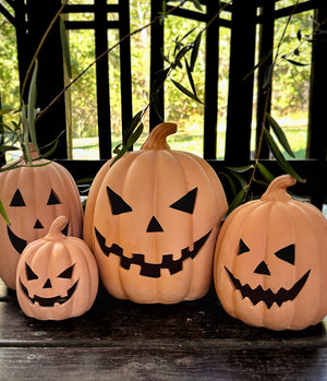 Four terracotta jack-o'-lantern on a wooden surface with green leaves in the background