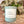 Candle with scent label 'Zen Garden' on a wooden surface surrounded by decorative rocks, plants, and a sprinkling of sand.