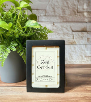 Snap bar wax melts in a black paper box with scent label ' Zen Garden'. Box is resting on a wooden surface with plant and white brick in the background. 