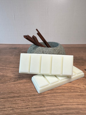 Two snap bar wax melts on a wooden surface leaning against a gray rock with wooden sticks.